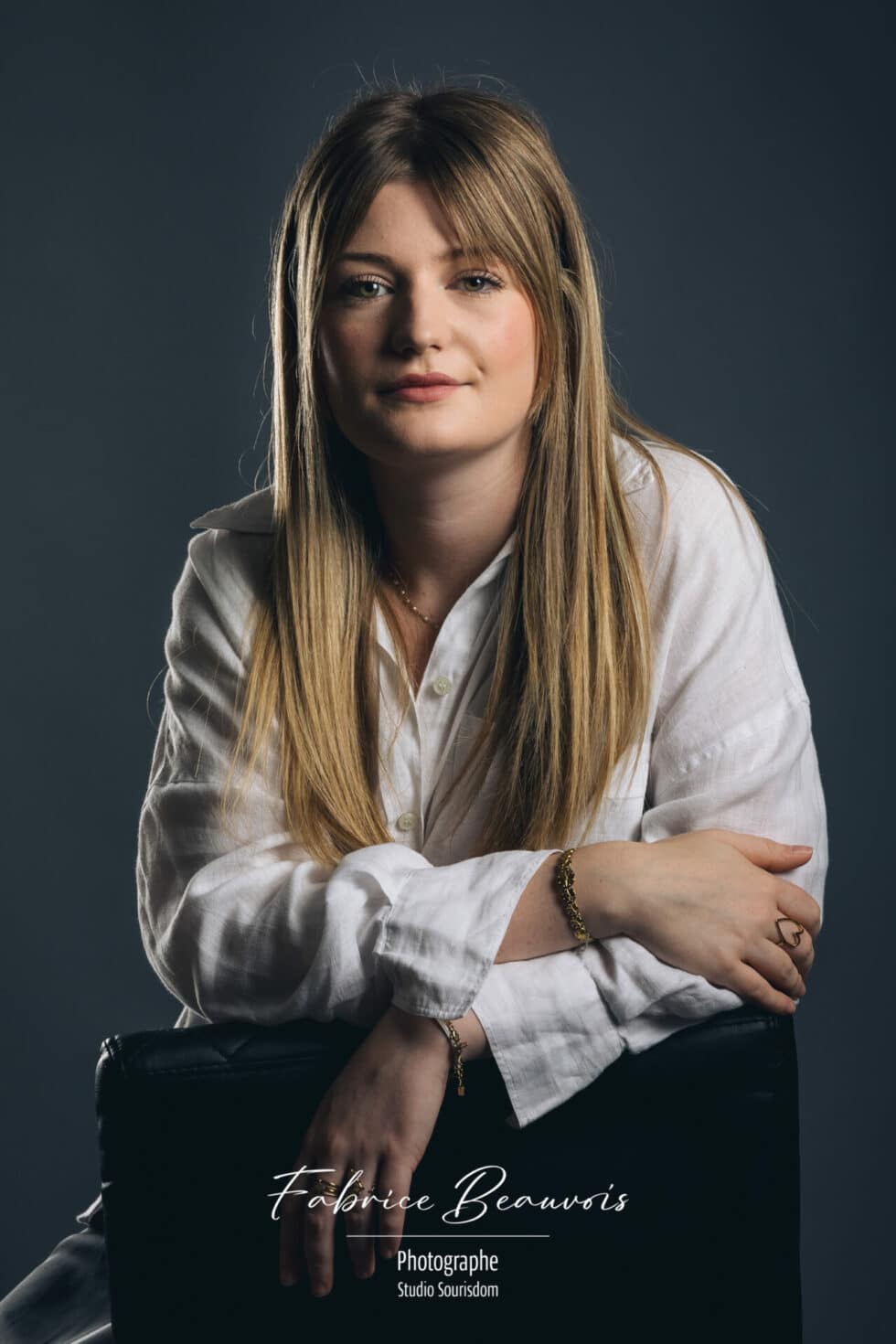 Portrait studio de face bras croisés sur un siège dans une ambiance grise bleutée