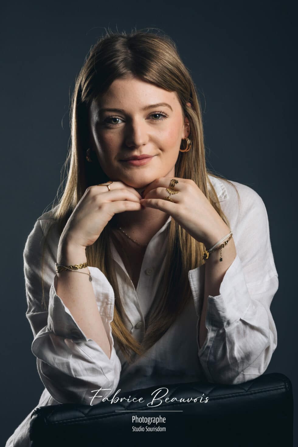 Portrait de face dans une ambiance gris bleuté avec les mains positionnées sous le menton